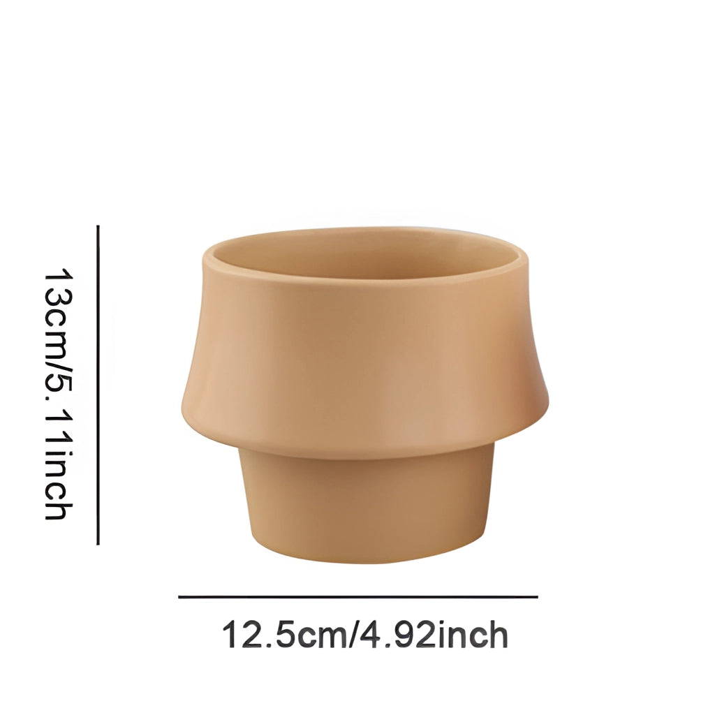 A ceramic planter in a rosa color with a glazed finish, showcasing a Scandinavian style, designed as a cylinder-shaped pot placed on a wooden surface.