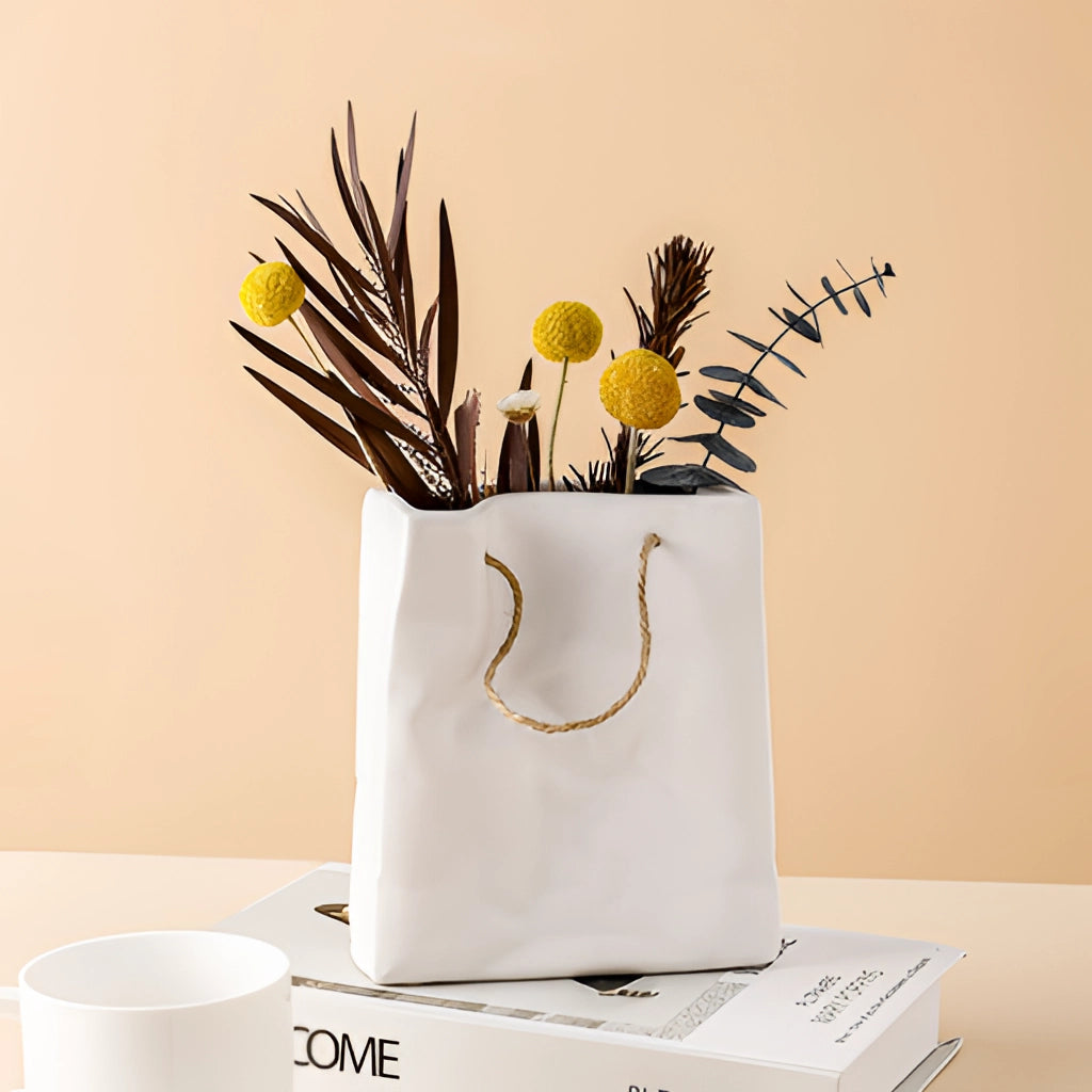 A ceramic vase decorated with a shopping basket design, possibly filled with twigs and small plants, displayed on a wooden surface.