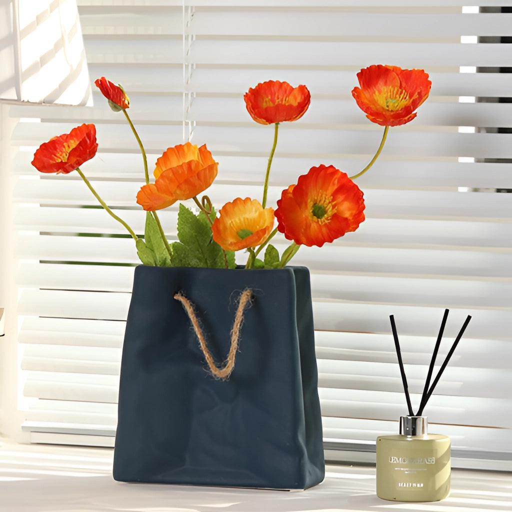 Ceramic vase with a shopping basket design, filled with orange flowers, displayed near a window in a stylish interior setting.