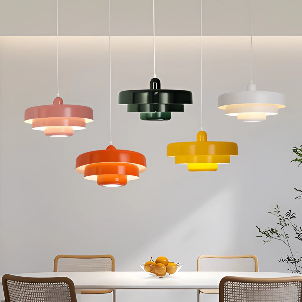 Modern metal pendant lamp with a circular design, hanging in a stylish interior with a white background, green and orange plants, and a yellow chair.