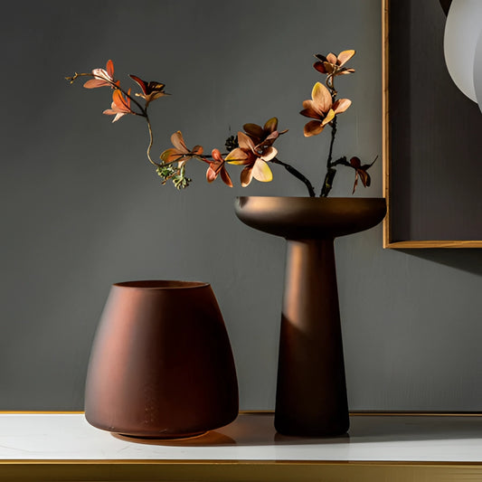 Coffee-colored frosted glass vase displayed on a wooden table with a light brown twig and plant arrangement.