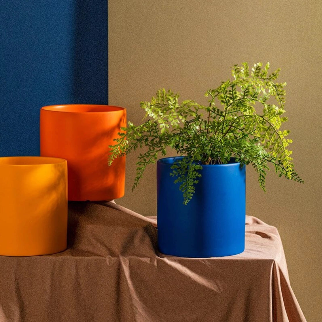 Colorful ceramic planter and saucer set with a green houseplant, placed on a wooden table in a stylish interior setting.