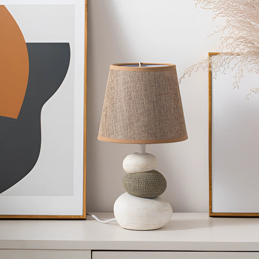 Contemporary fabric lampshade on a wooden desk, emitting a warm light, suitable for use on a desk or nightstand, with a rectangular shape and a minimalist design.
