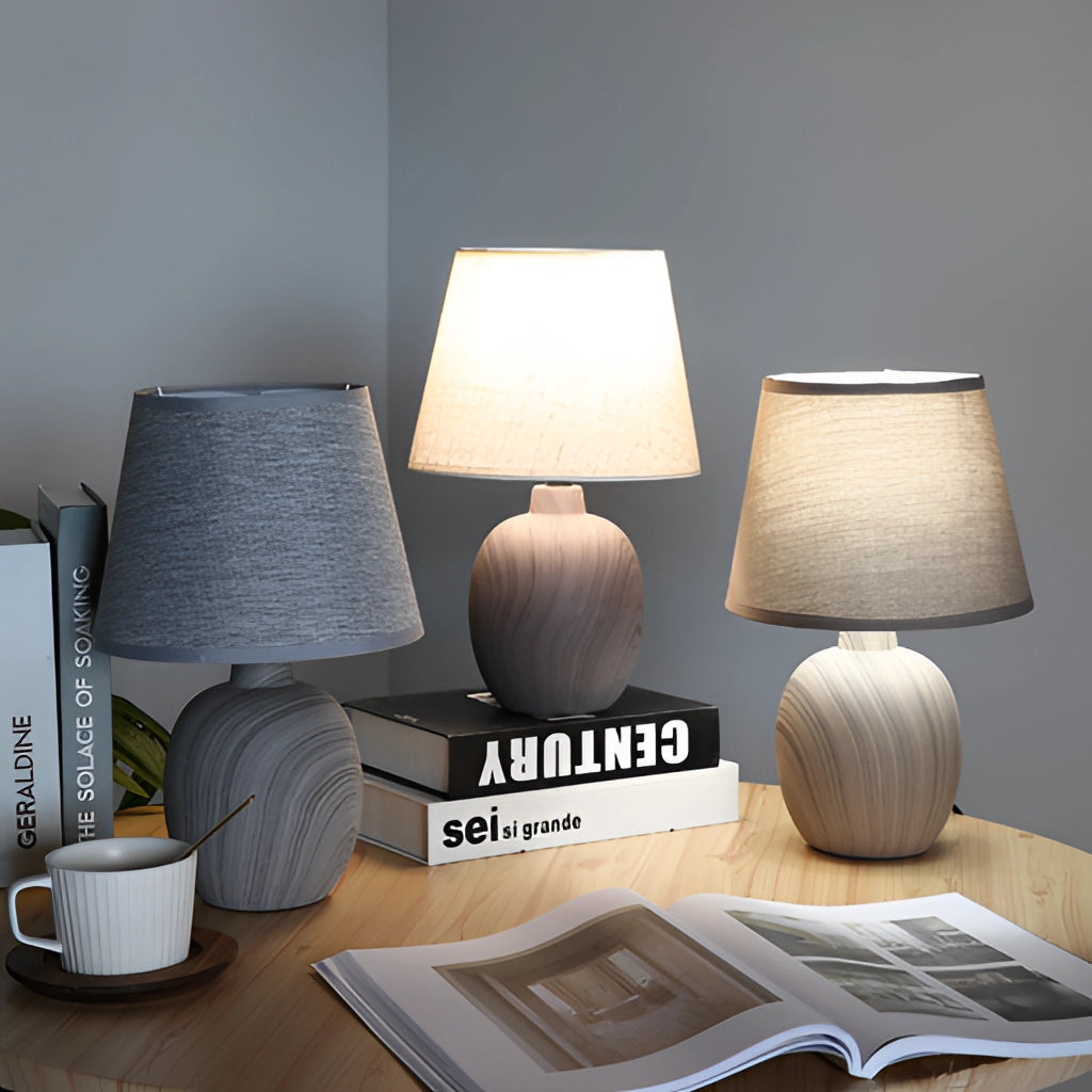 Contemporary rechargeable table lamp with a unique style, featuring a wooden base, grey textile shade, and placed in a cozy interior setting next to a book.