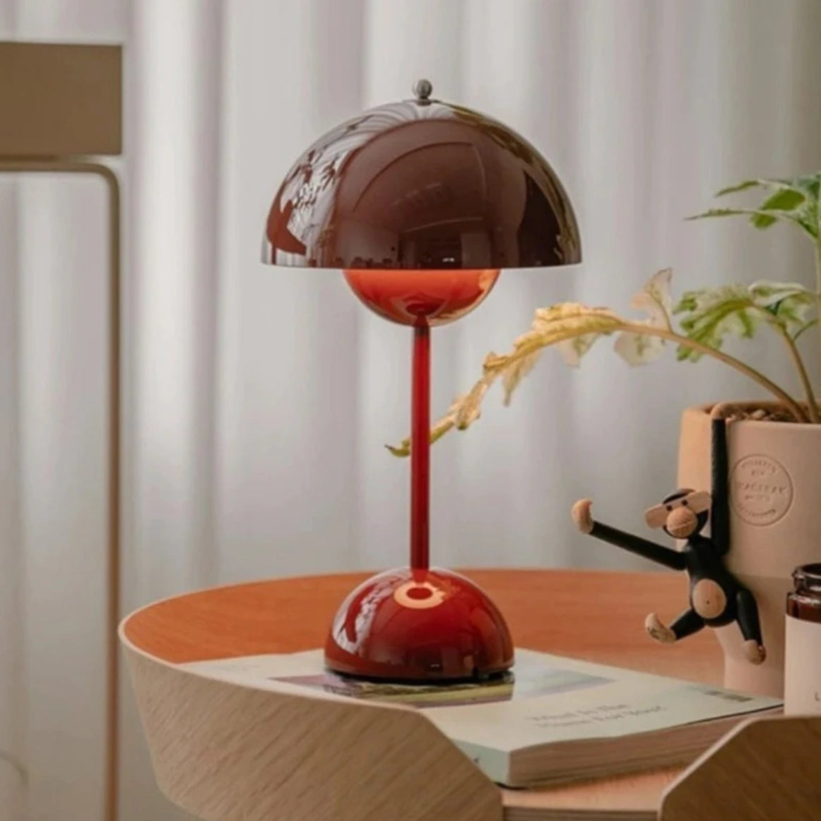 Cordless orange flowerpot table lamp with touch sensor, placed on a wooden shelf in a modern interior setting.