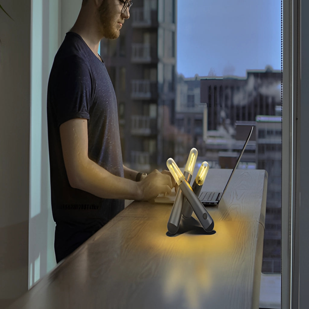 A sleek cordless LED table lamp with a kinetic rotation feature, positioned on a table, with a person in a T-shirt and eyewear making a gesture beside it.