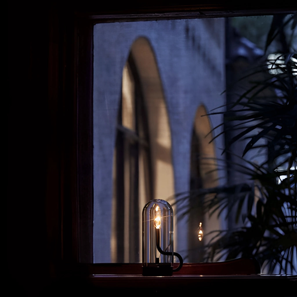 Cordless LED table lamp on a modern interior table near a large window with a view of a building facade, curtains partially drawn, and trees in the background.