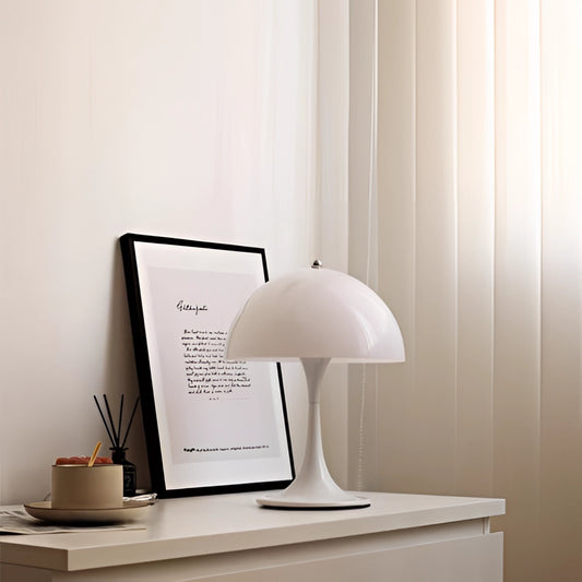 Cordless LED table lamp with rechargeable battery on a wooden desk next to a computer and potted plant in an office setting.