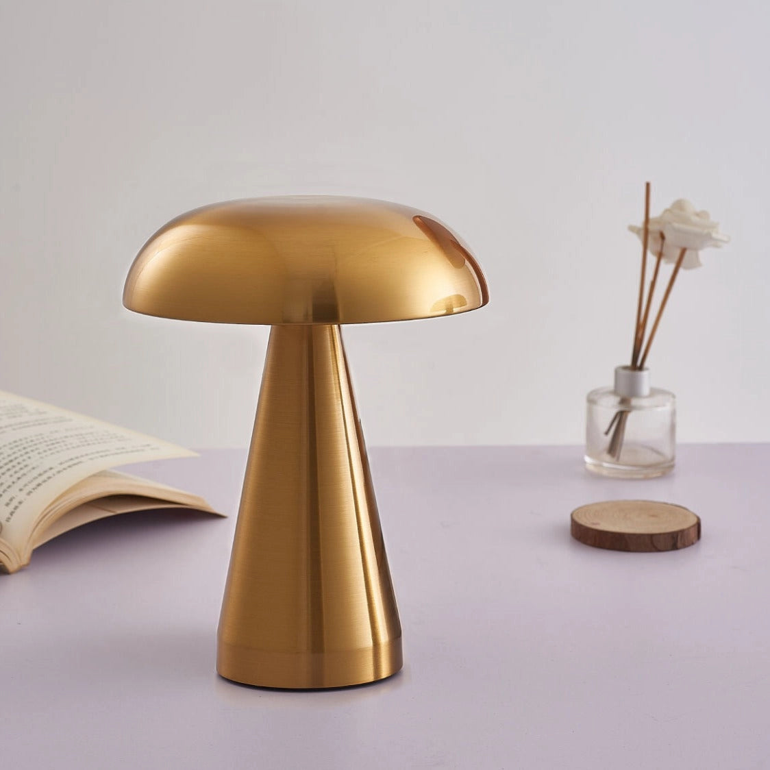 Cordless Mushroom LED Table Lamp with steepless dimming in brass finish, placed on a wooden table with a chair nearby, featuring a sleek metal base and a soft, tints and shades lampshade.