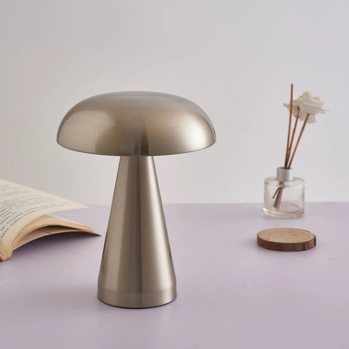 Cordless silver mushroom LED table lamp with steepless dimming, placed on a wooden table, surrounded by minimalist furniture.