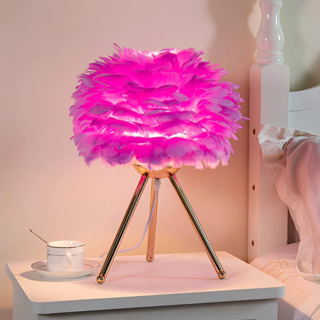 Feather LED Table Lamp with dimmable lighting in the Lila variant, featuring a purple and pink feather design, placed on a table beside a plant and flower.