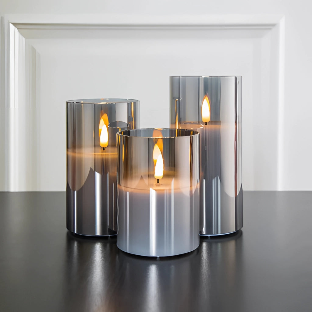 Three-piece flameless glass candle set with remote control, featuring LED pillar candles placed on a table alongside a small plant and drinkware.