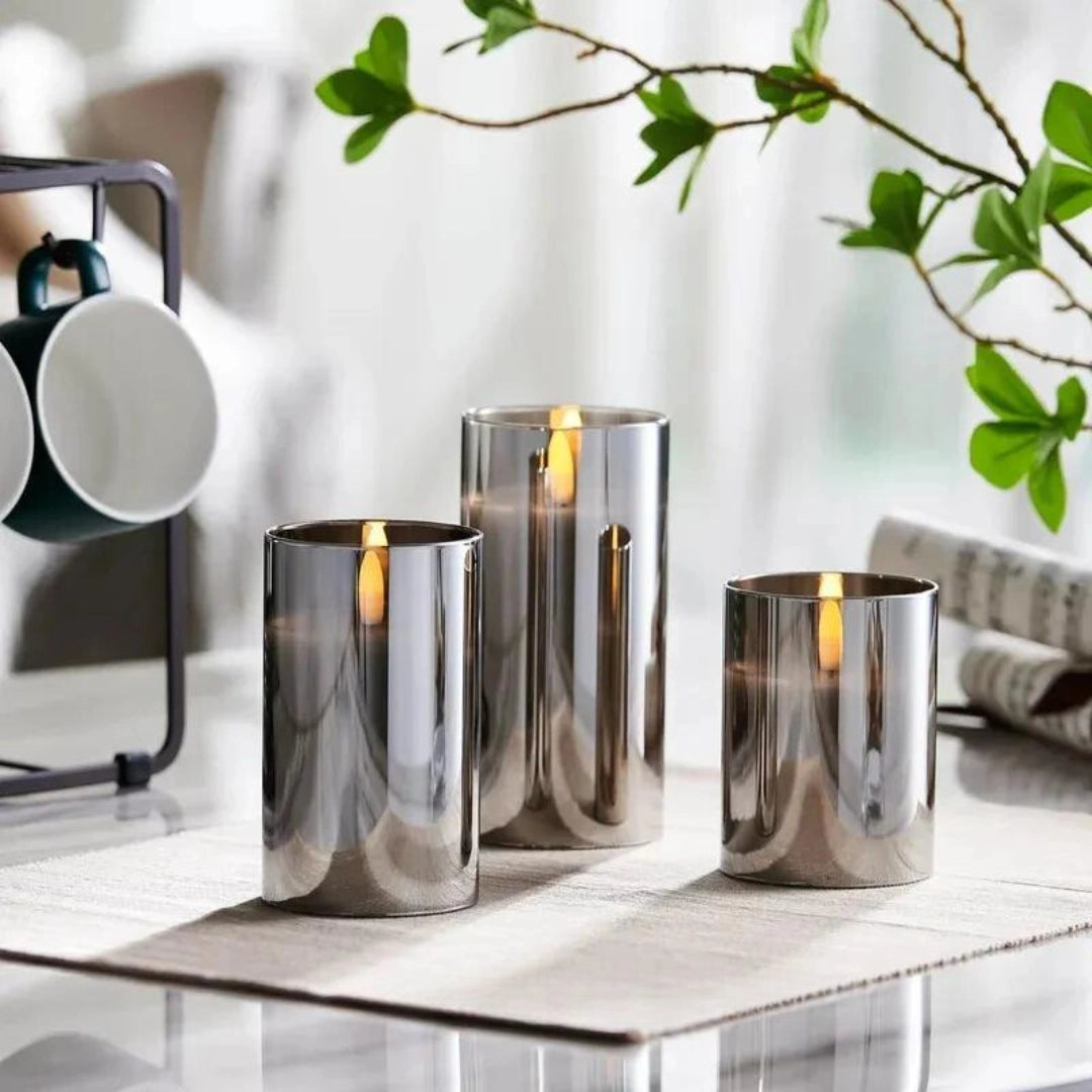 Three-piece flameless glass candle set with remote control on a wooden table, surrounded by plants and interior decor.