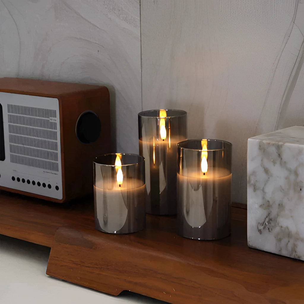 Set of three flameless glass LED pillar candles with remote control, featuring a realistic wax appearance and placed in glass holders.
