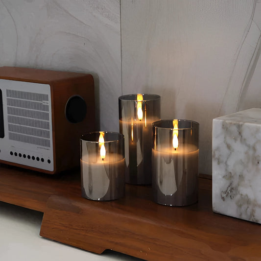Set of three flameless glass LED pillar candles with remote control, featuring a realistic wax appearance and placed in glass holders.
