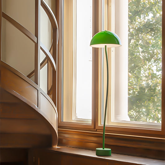 A floor lamp with an organic design, featuring quality craftsmanship and tricolor lighting in green, white, and another hue, placed near a window with a wooden shade and surrounded by plants in a modern interior setting.