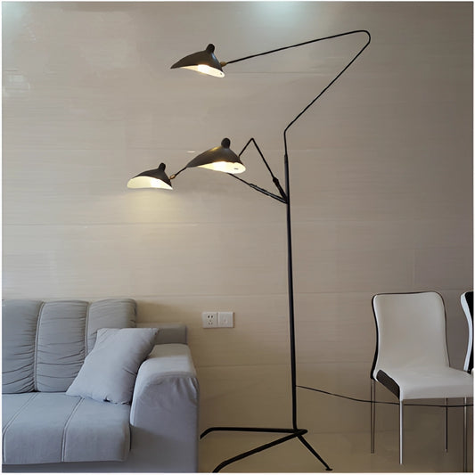 A floor lamp with a tripod base and directional light, featuring a grey lamp shade, standing next to a comfortable grey couch and chair in a modern living room.