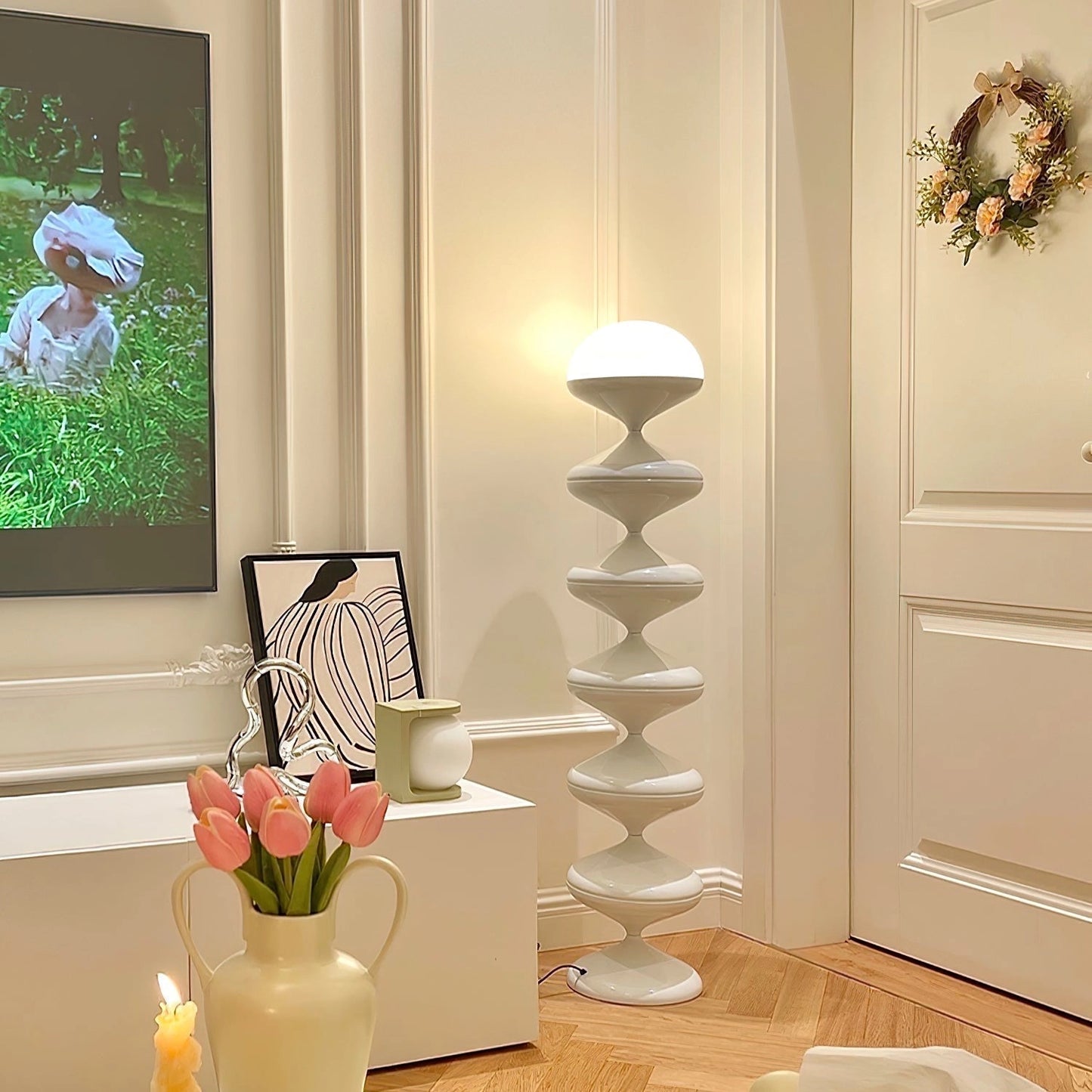 Modern floor lamp with twisted gourd design, white color, placed in an elegant interior setting with a table, vase, plant, picture frame, and wooden floor.