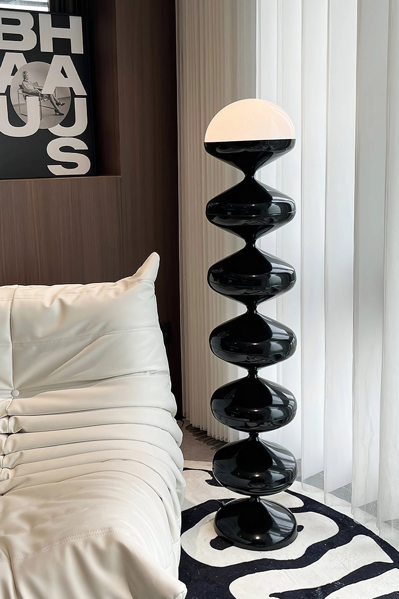 Modern white floor lamp with twisted gourd design, placed in a cozy interior setting featuring hardwood floors, a wooden shelf, and a comfortable pillow.
