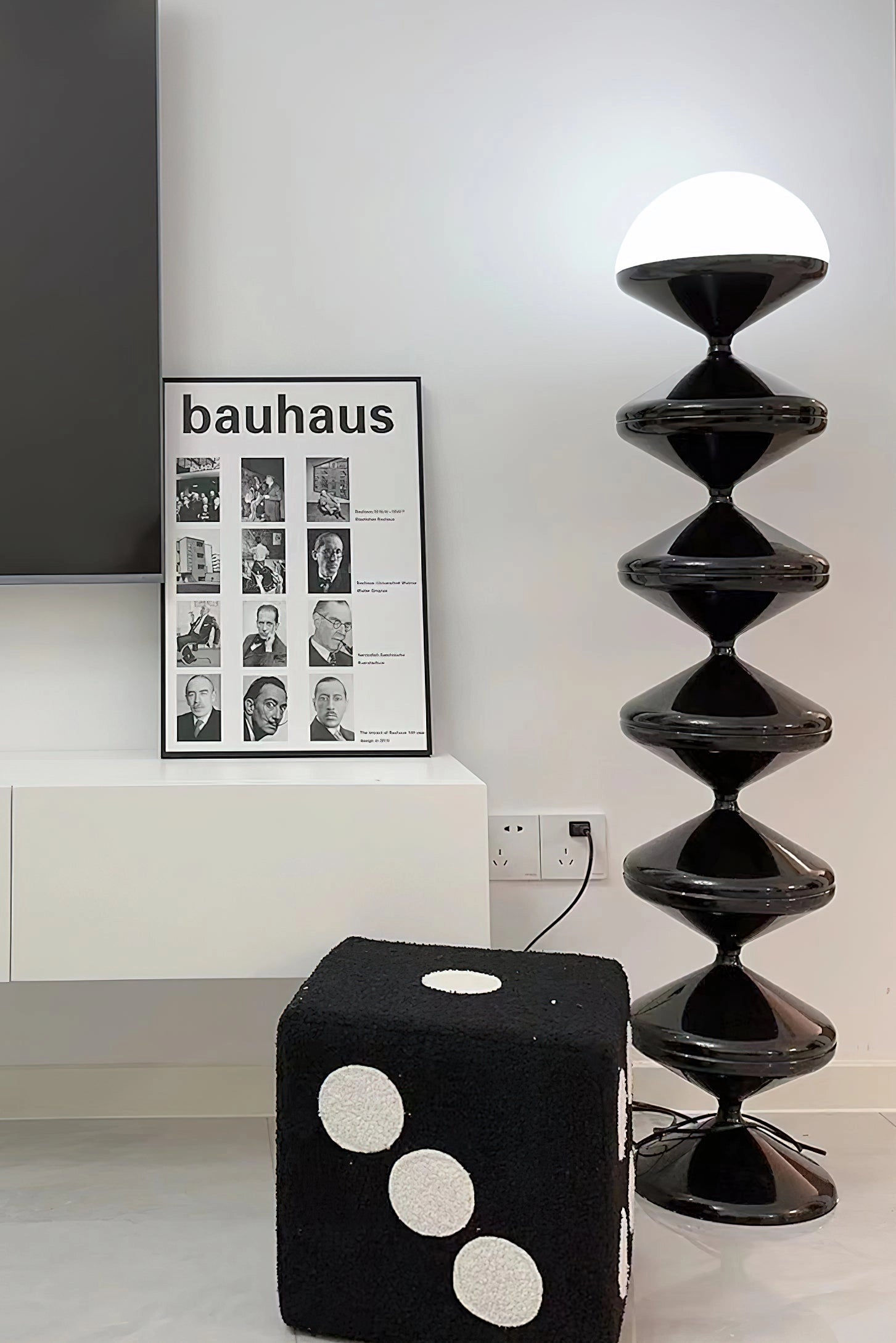 Modern floor lamp with twisted gourd design, featuring a white and black color scheme, placed in a stylish interior with grey walls, wooden shelves, and contemporary art.