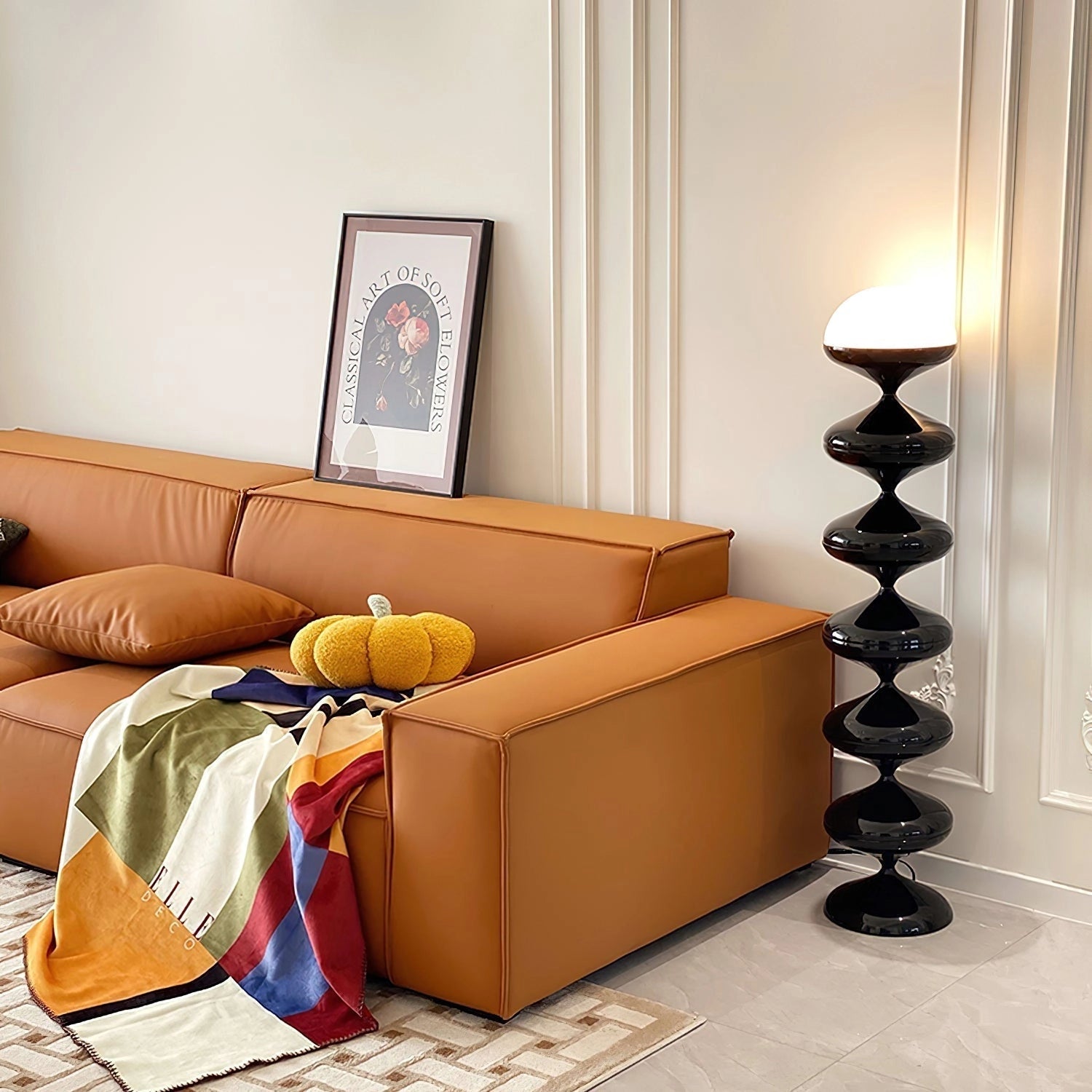 Modern elegant floor lamp with twisted gourd design placed in a stylish living room with a comfortable couch, wooden flooring, and framed pictures on the wall.