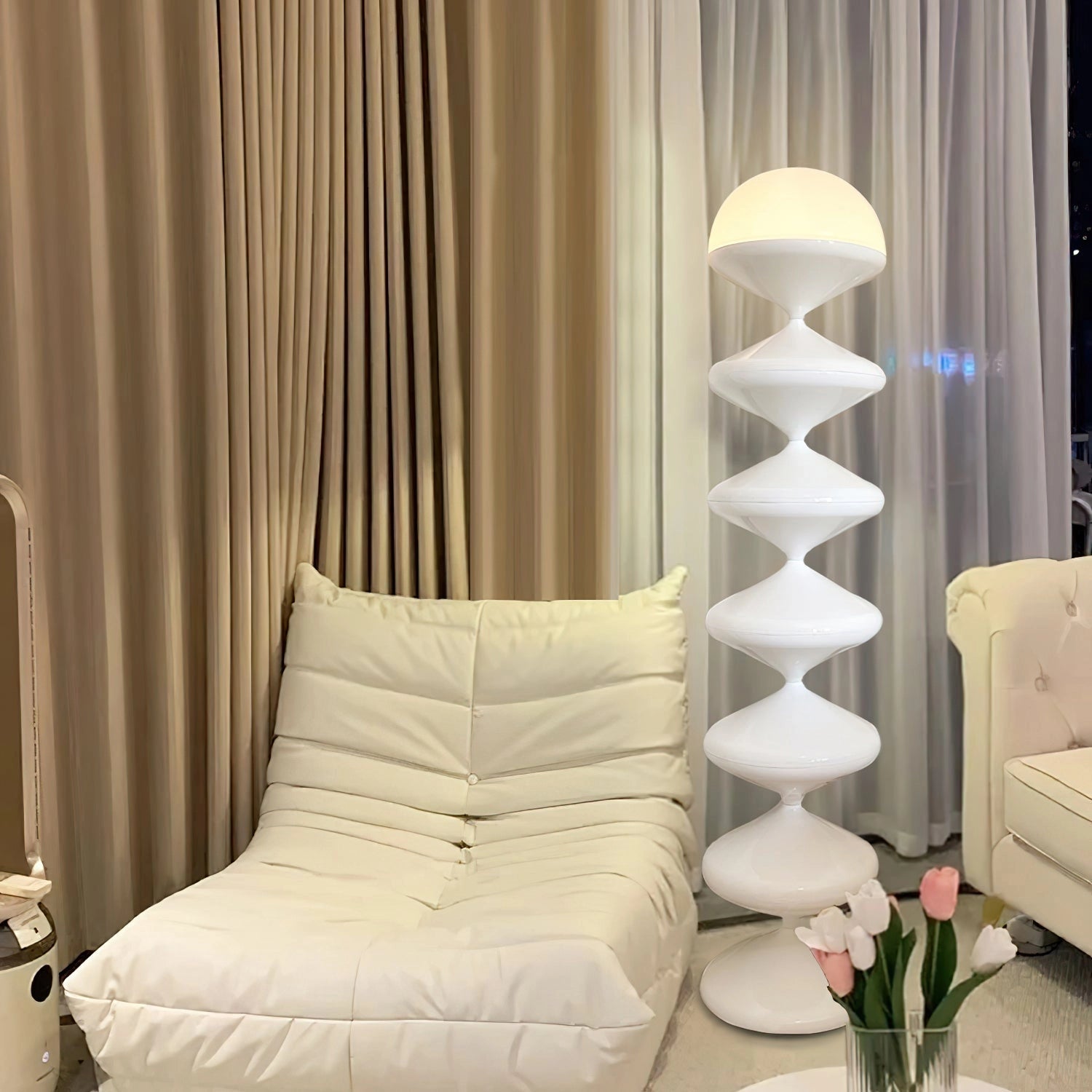 Modern elegant floor lamp with twisted gourd design, featuring a sleek shade, positioned in a cozy and stylish interior setting with wooden flooring, textiles, and nearby plants and pillows.