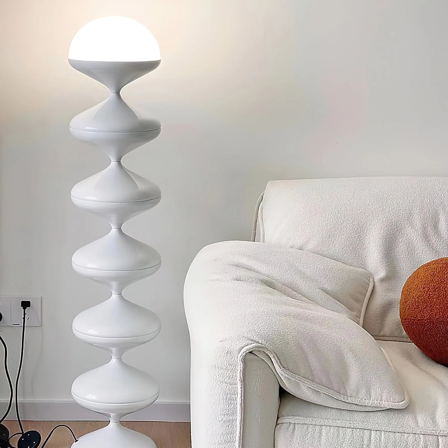 Modern floor lamp with twisted gourd design in grey, placed in a cozy living room with a wooden floor and a grey studio couch.