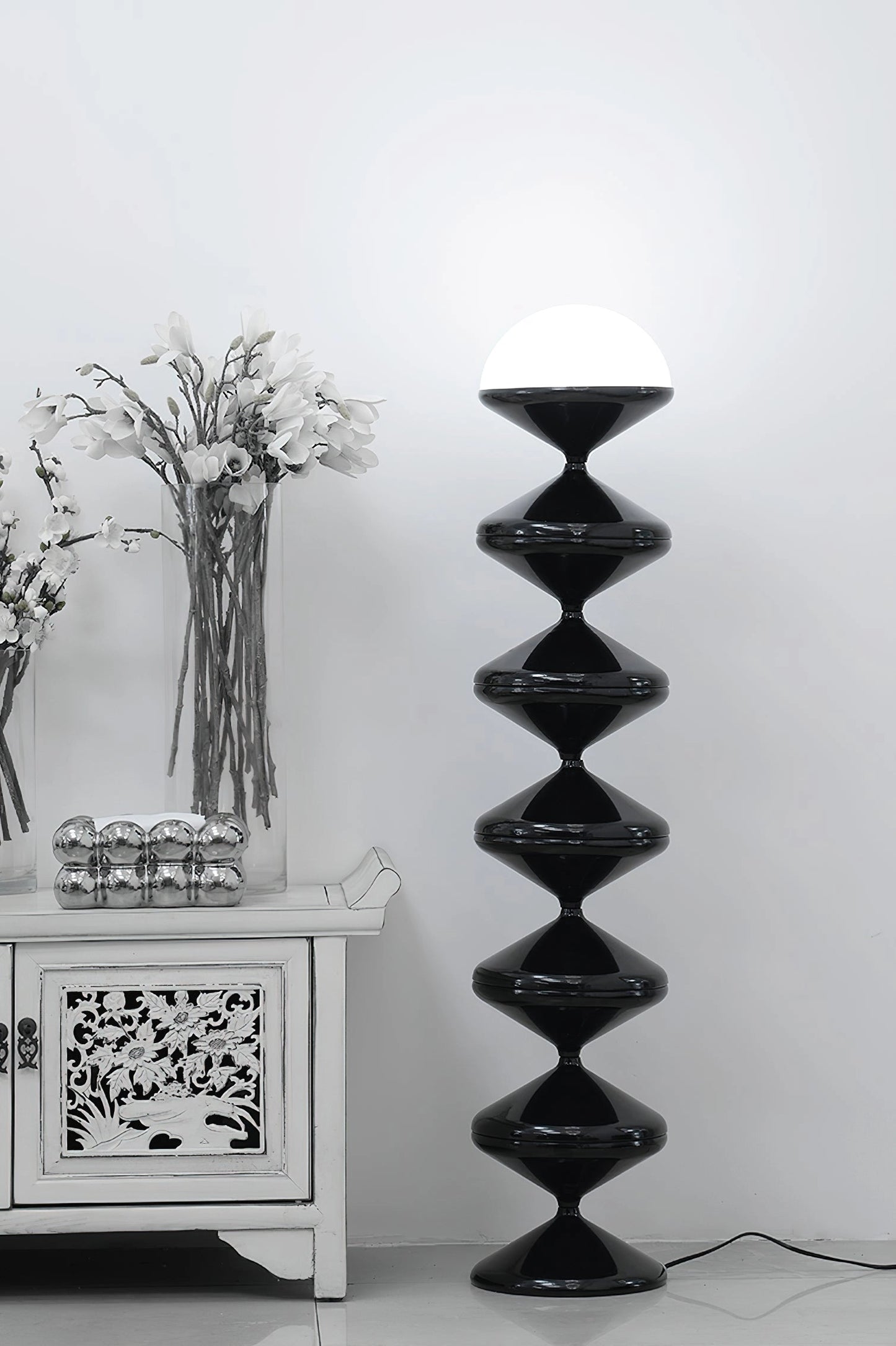 Modern elegant floor lamp with twisted gourd design, surrounded by wooden shelves and decorative plants.