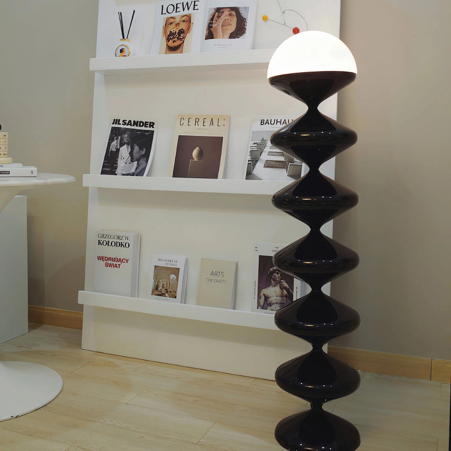 A modern elegant floor lamp with a twisted gourd design, placed on hardwood flooring in a living room next to a wooden bookshelf.