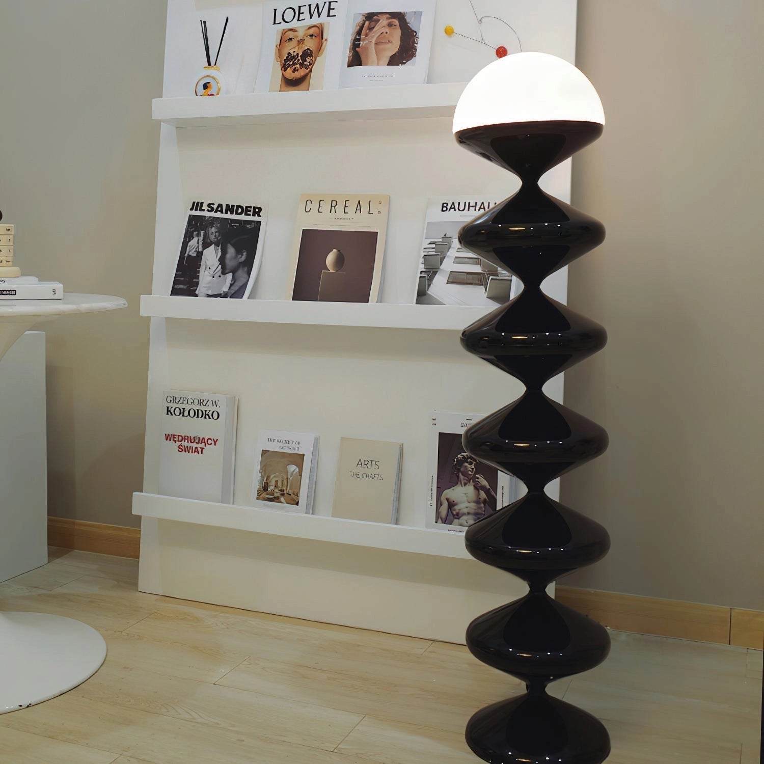 A modern elegant floor lamp with a twisted gourd design, placed on hardwood flooring in a living room next to a wooden bookshelf.