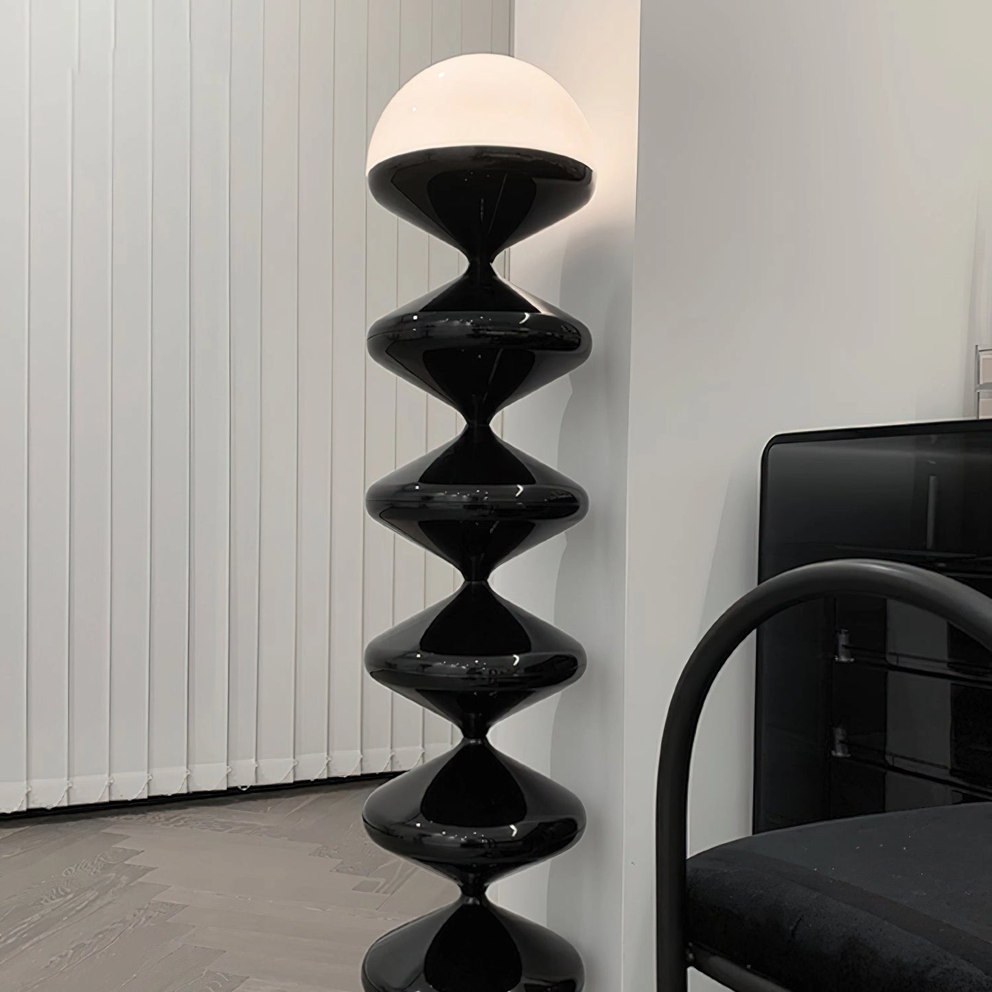 Modern elegant floor lamp with twisted gourd design, placed on hardwood flooring near a wooden shelf and metal chair.