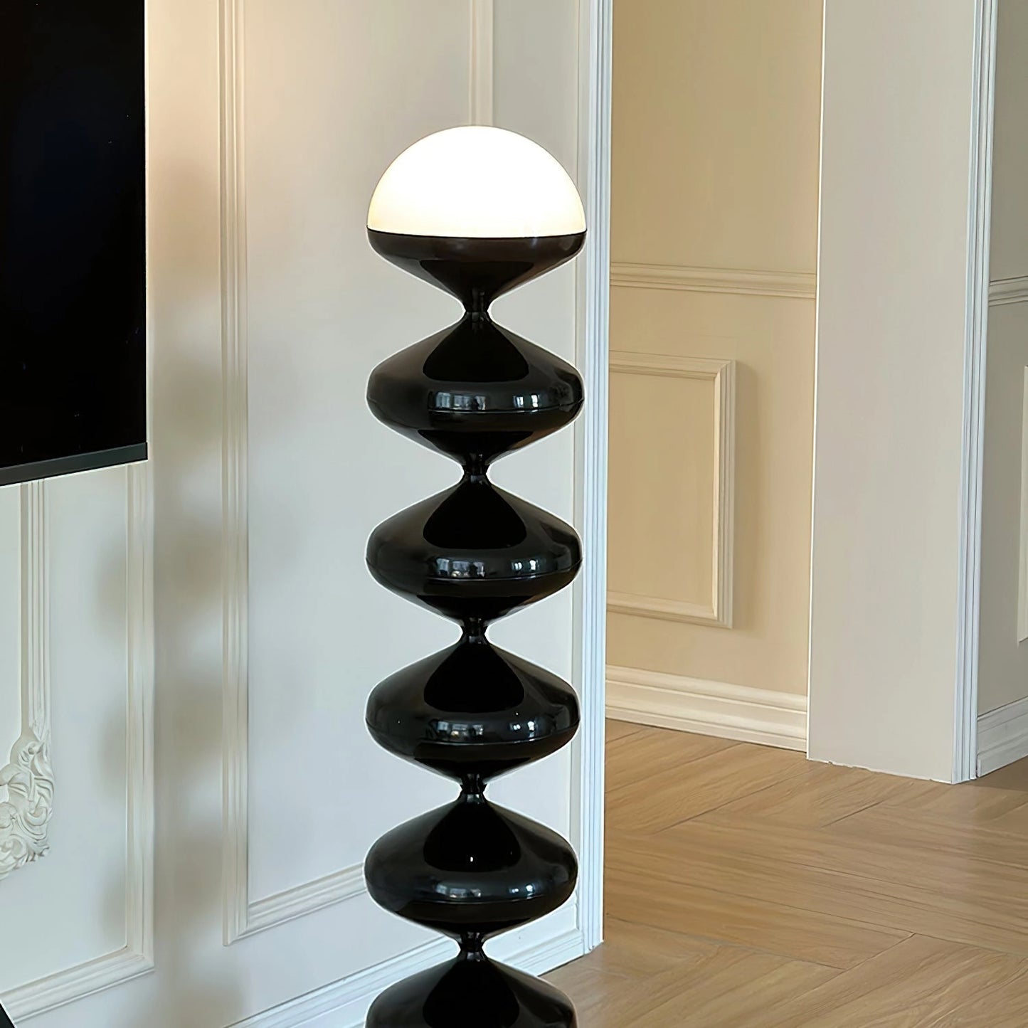 Modern floor lamp with twisted gourd design next to wooden shelving unit and hardwood flooring.