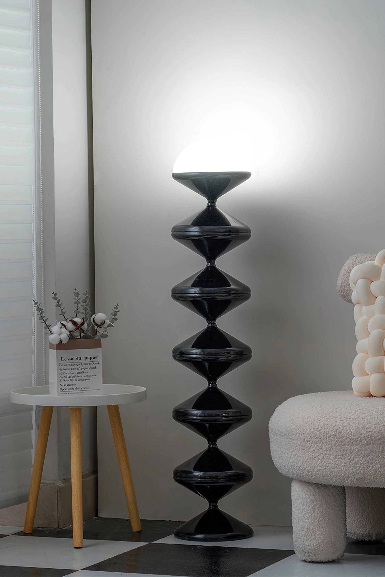 Modern elegant floor lamp with twisted gourd design standing next to a wooden shelf with picture frames, plants, and decorative items, enhancing a grey interior design.