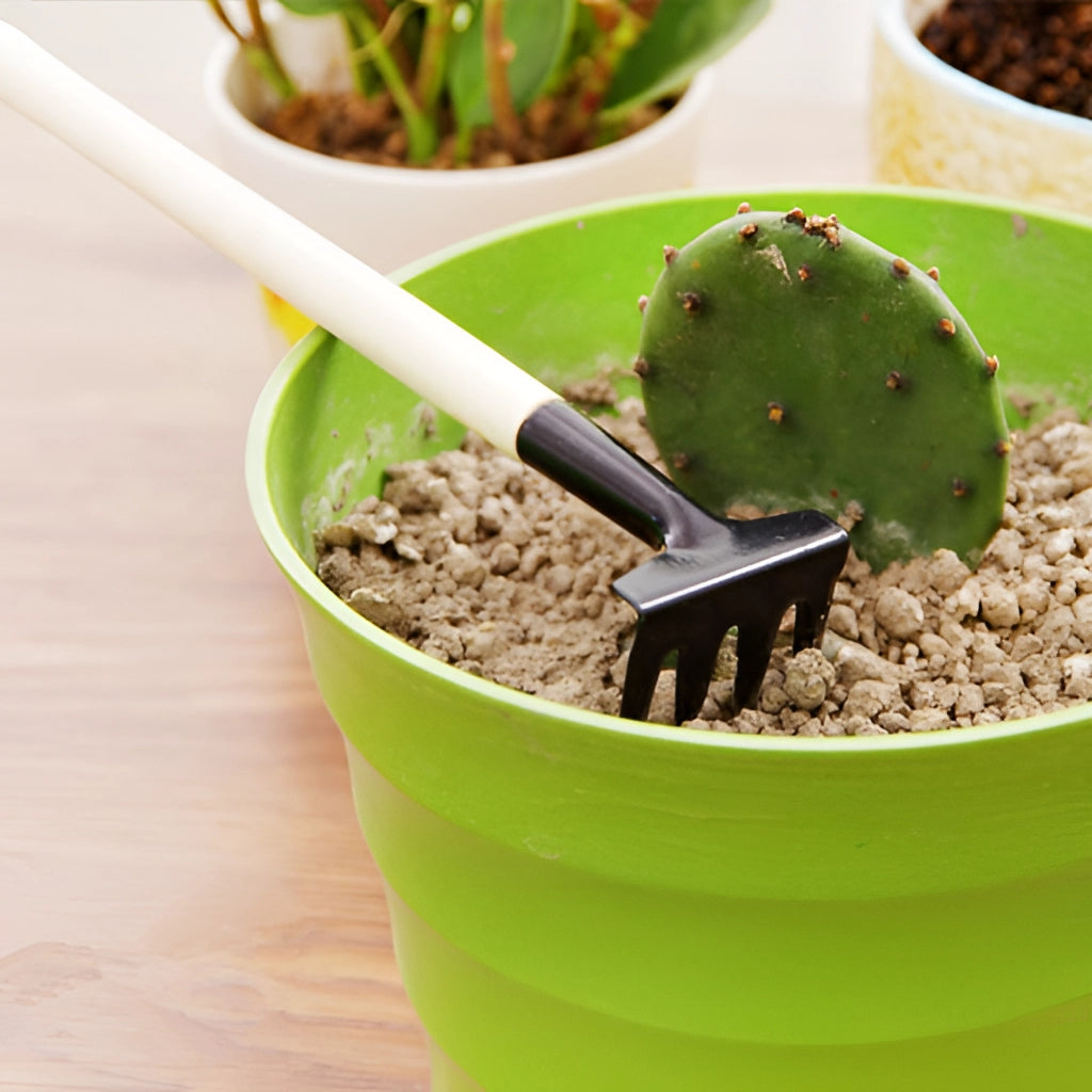 Gardening tool set with durable iron and wood handles placed next to a flowerpot with soil and an assortment of plants.