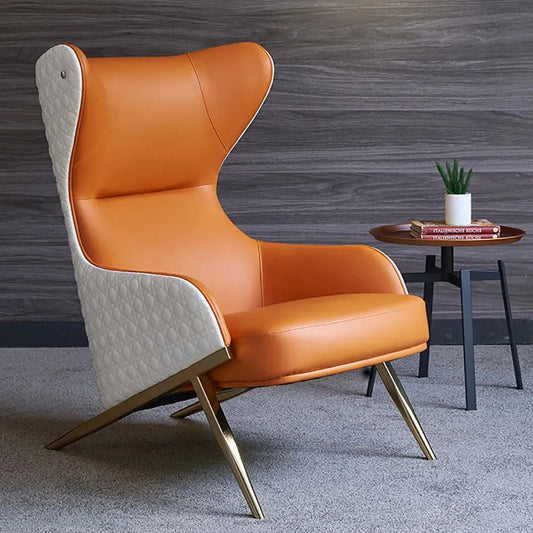 Orange geometric wingback accent chair with a gold trestle base, featuring armrests and comfortable cushioning, displayed on a wooden floor with a plant in the background.