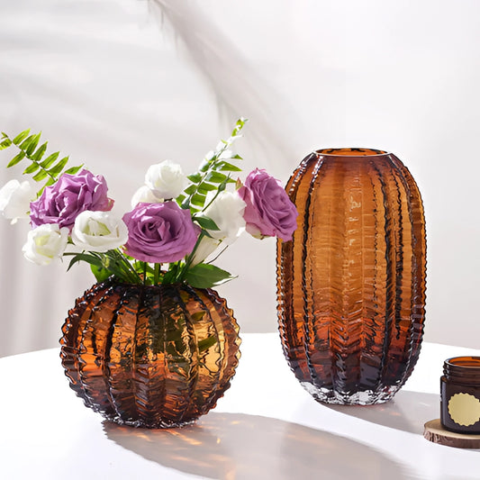 Glass cactus vase with artificial purple flowers arranged in a decorative display on a table.