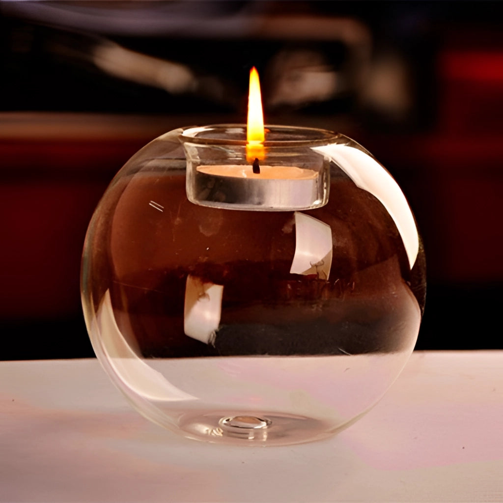 Glass candle holder with a burning tealight, orange flame casting warm light.