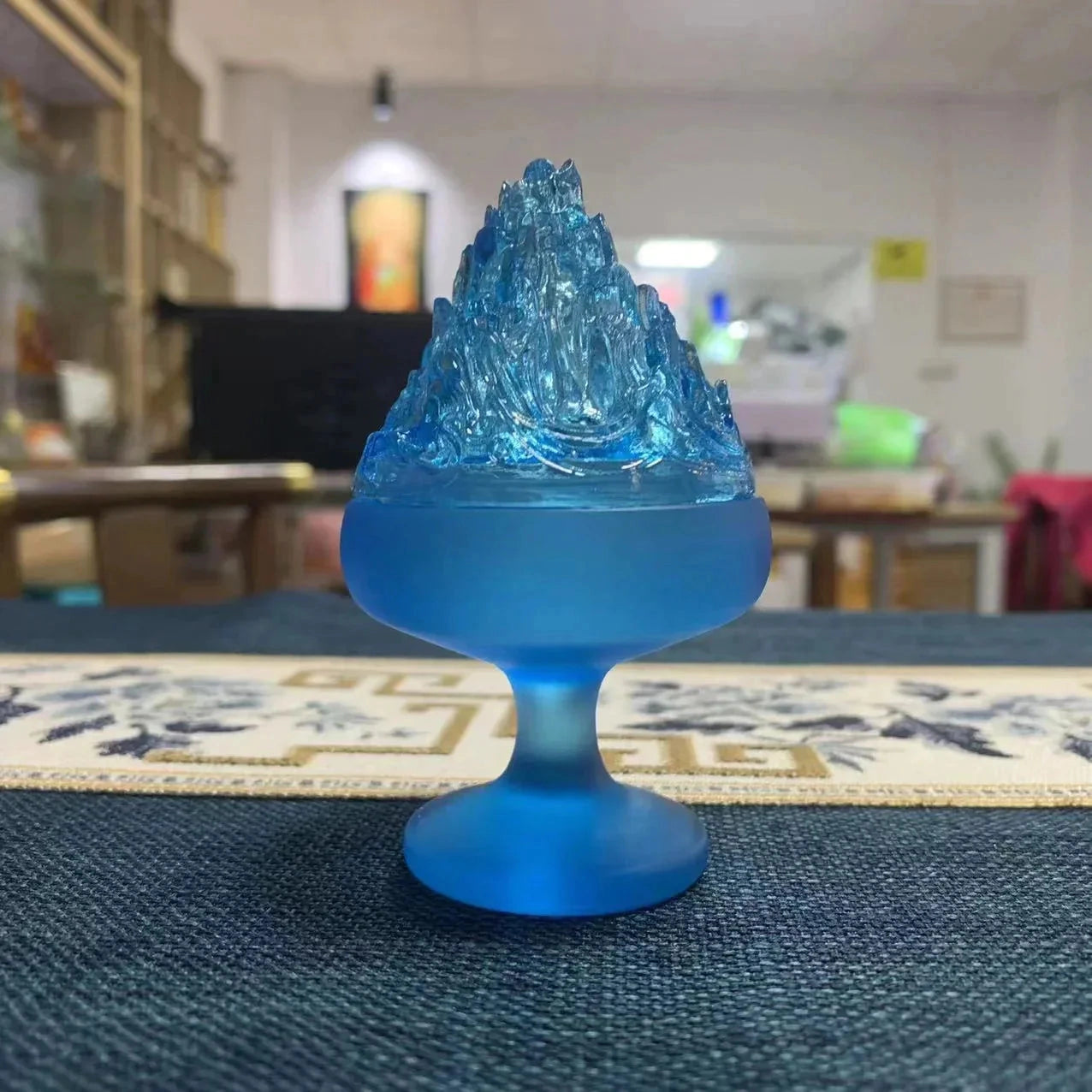 A blue glass incense burner with a cone-shaped design sits on a wooden surface, ideal for Zen home decor.