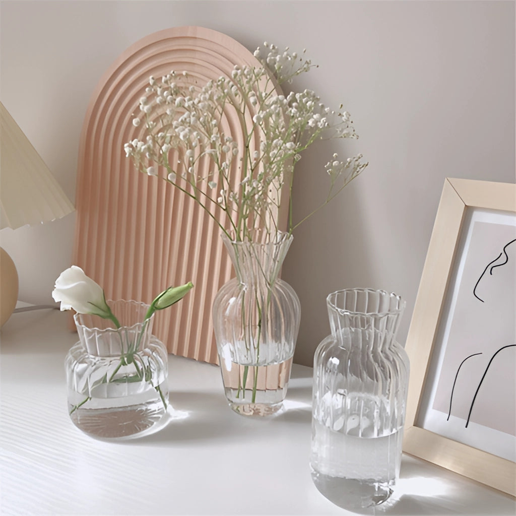 Nordic style transparent glass plant vase with branches placed on a wooden table against a grey wall.