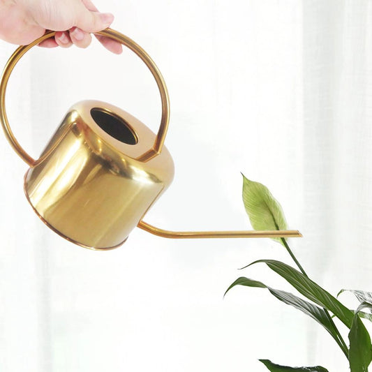 Gold stainless steel watering can placed next to various green plants and flowers.