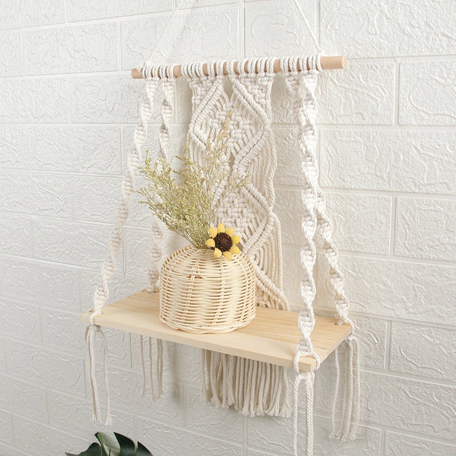 Handwoven macrame boho wall hanging tapestry with geometric art decor, displayed above a wooden table and chairs, accented with natural branches and twigs.