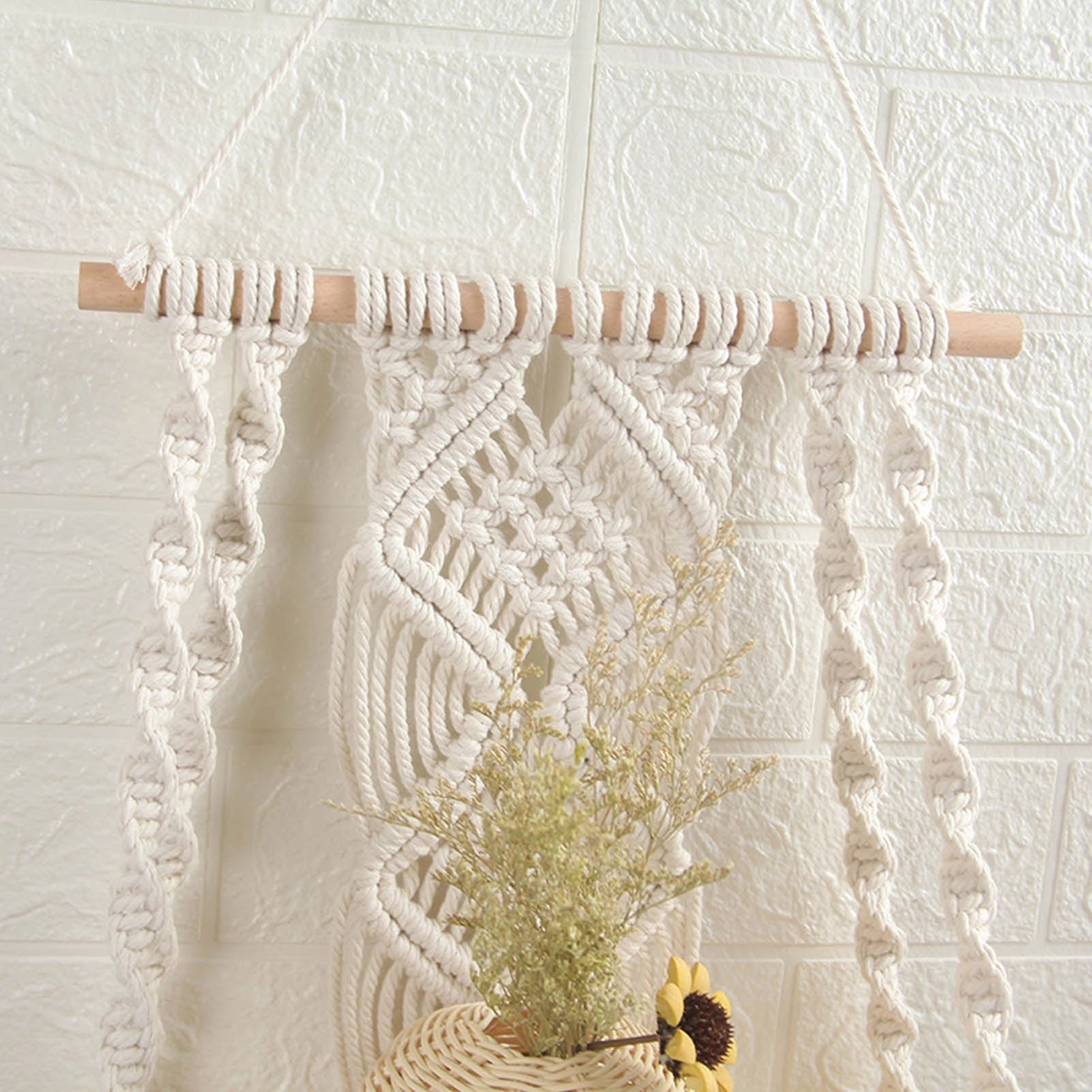 Handwoven macrame boho wall hanging tapestry featuring geometric art decor in white and beige tones, displayed against a wooden background with a small plant nearby.