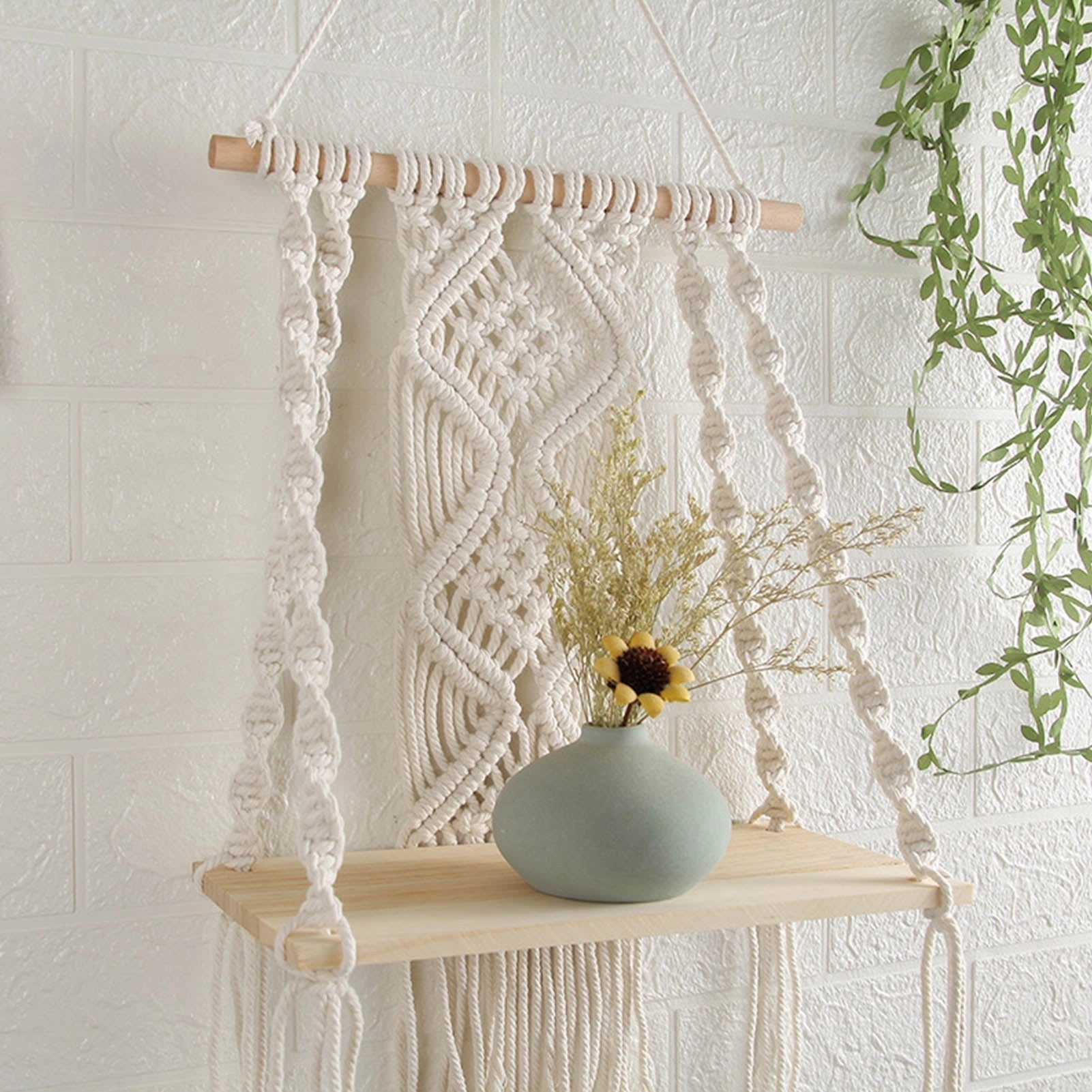 Handwoven macrame boho wall hanging tapestry in beige with geometric patterns, embellished with natural materials, displayed on a wooden shelf.