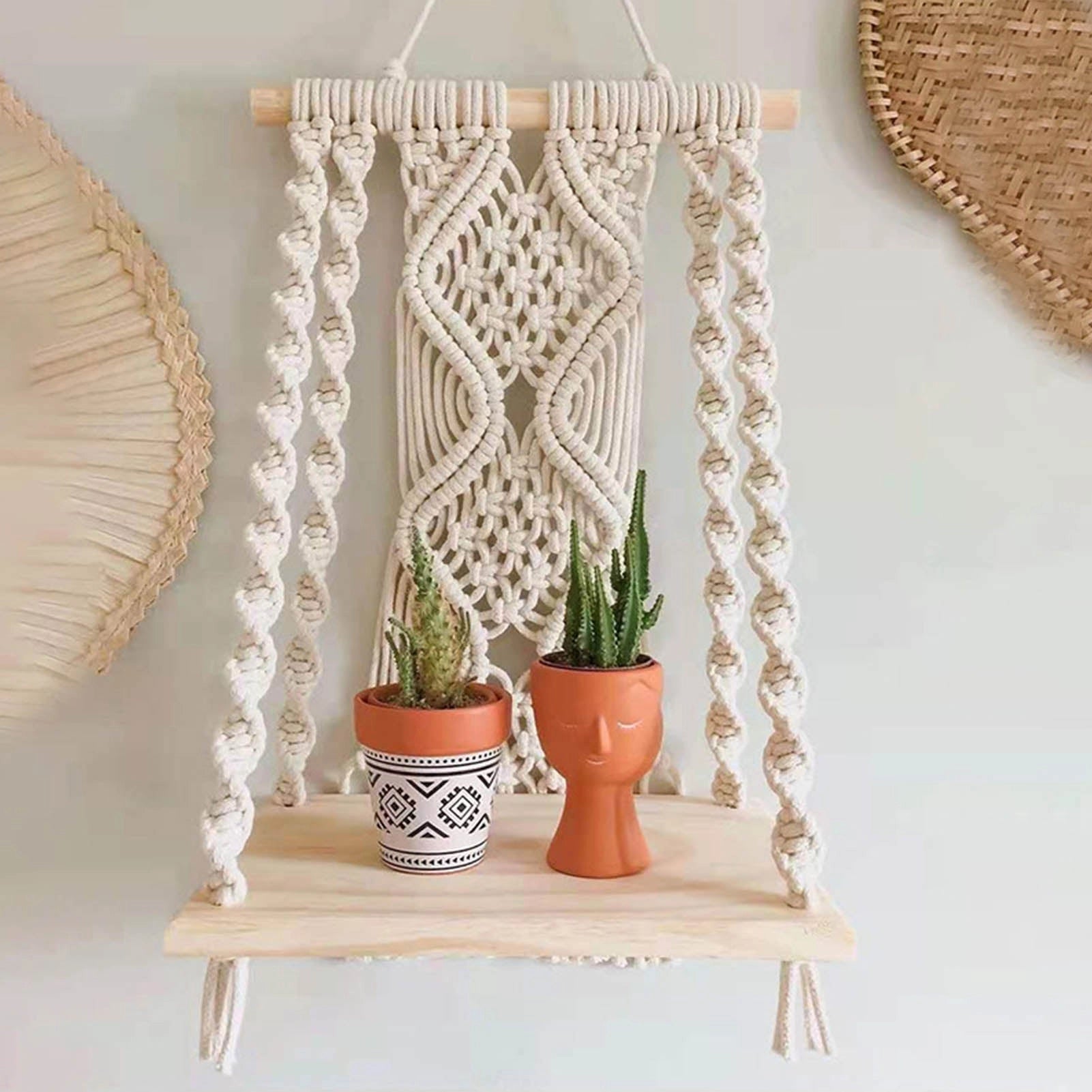 Handwoven macrame boho wall hanging tapestry with geometric art design displayed above a wooden shelf with houseplants and decorative ornaments.