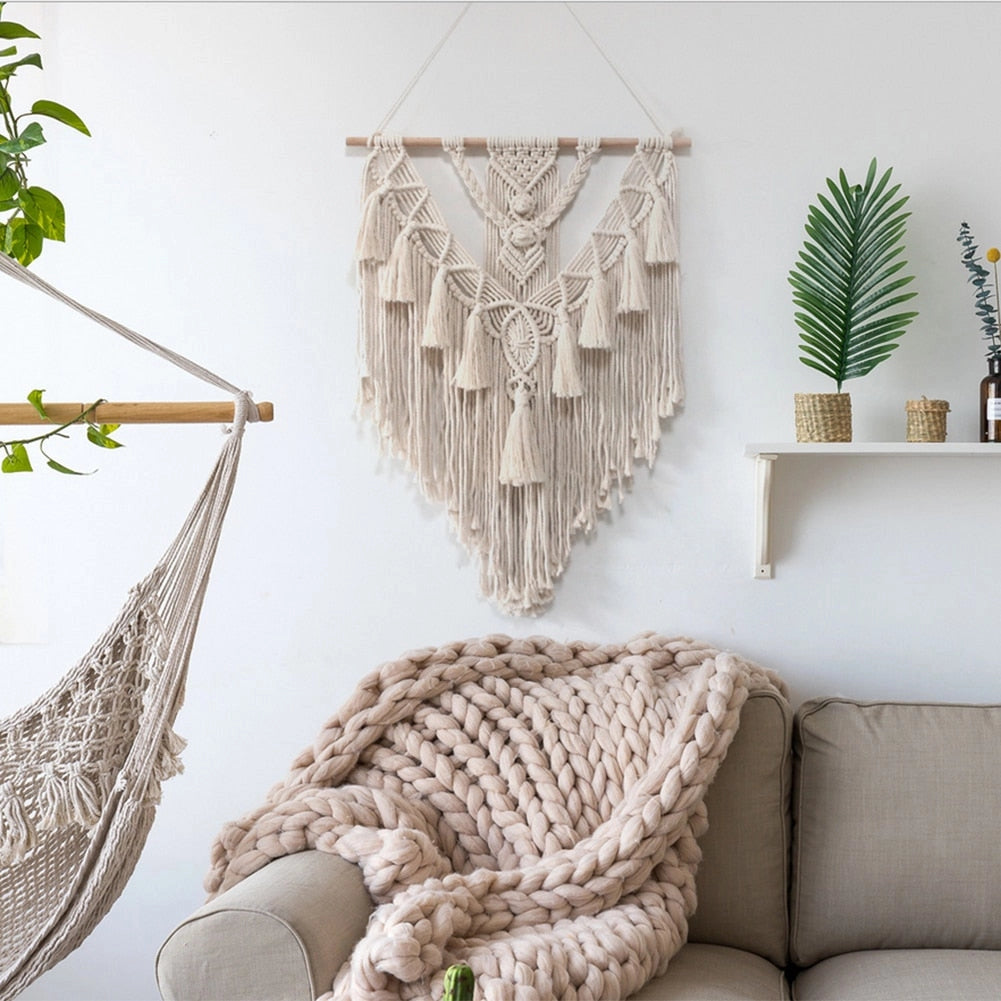 Handwoven macrame boho wall hanging tapestry with geometric art design, displayed on a white wall above a wooden couch, complementing the interior decor.