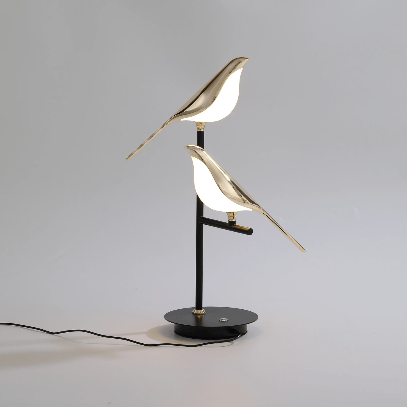 A stylish LED desk lamp featuring a postmodern design with a galvanized golden bird perched on a wooden twig.
