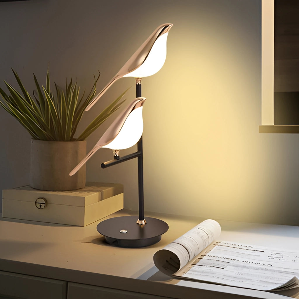 Postmodern LED desk lamp with a galvanized golden bird design on a wooden table surrounded by office supplies and a small plant in a well-lit interior setting.