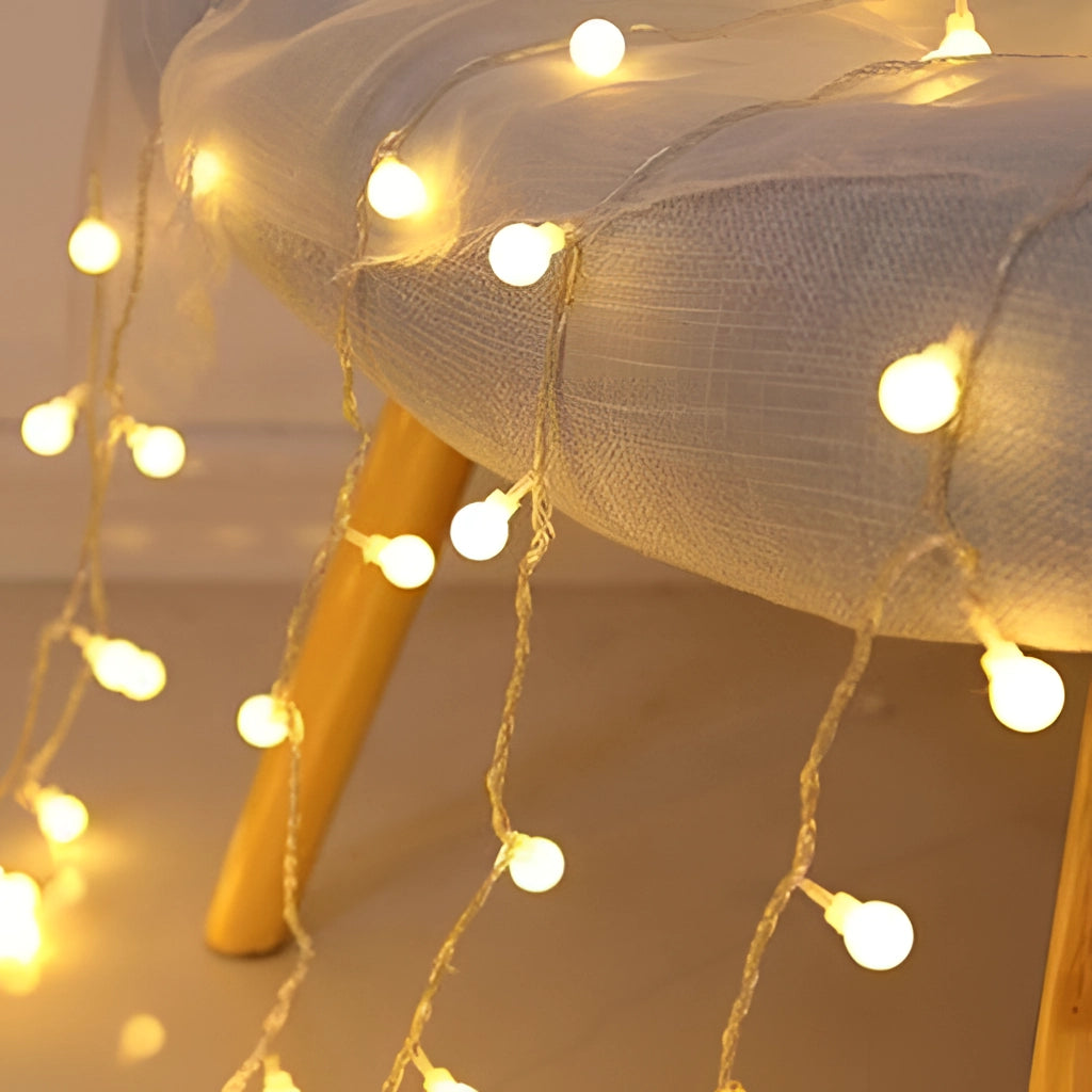 Warm white LED fairy string lights with 100 ball-shaped bulbs, creating a twinkling effect and a romantic ambiance, hanging from a wooden ceiling.