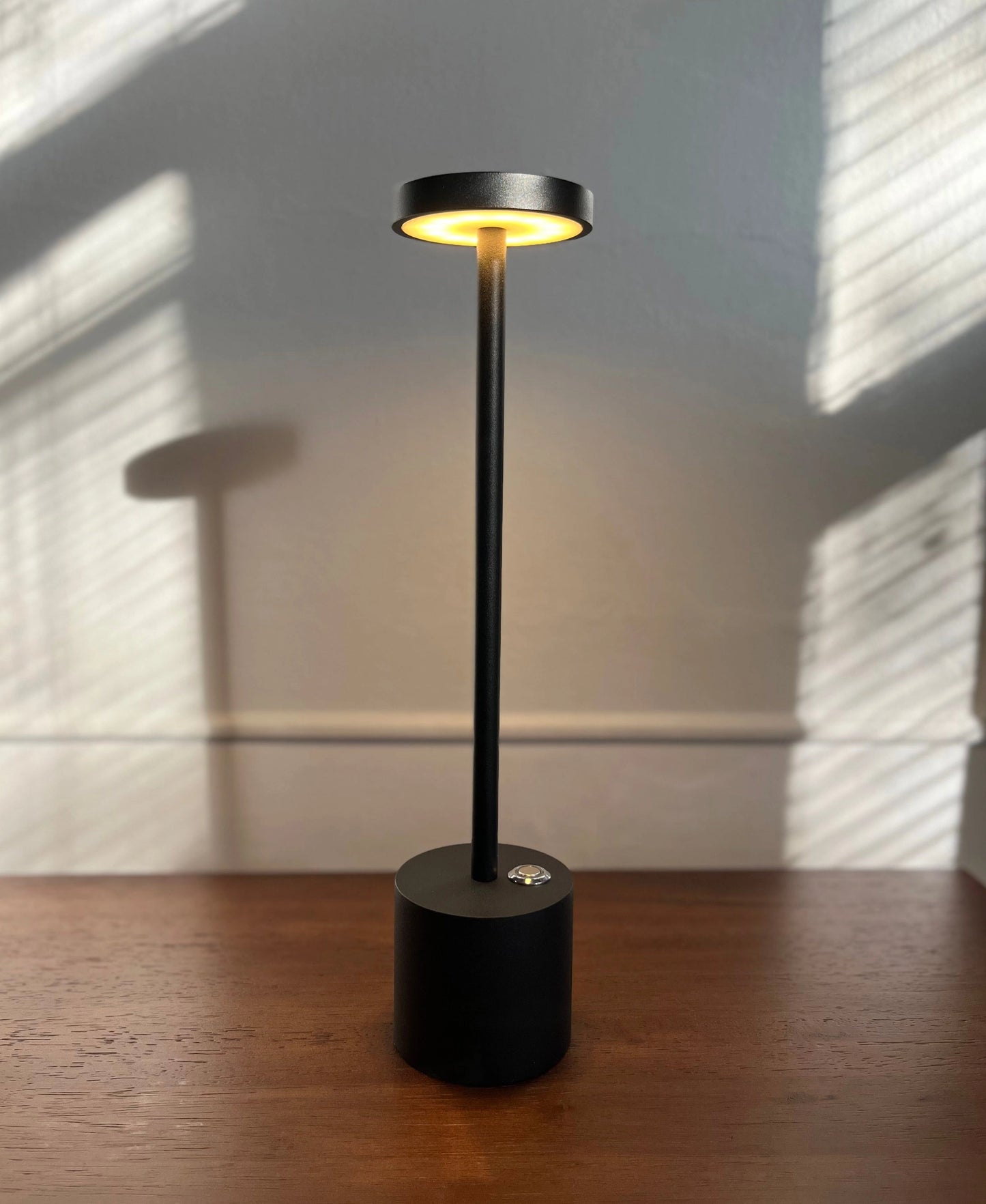 LED Portable Table Lamp with Resilient Design featuring a wooden base and circular lampshade, placed on hardwood flooring with ceiling fixture visible in the background.