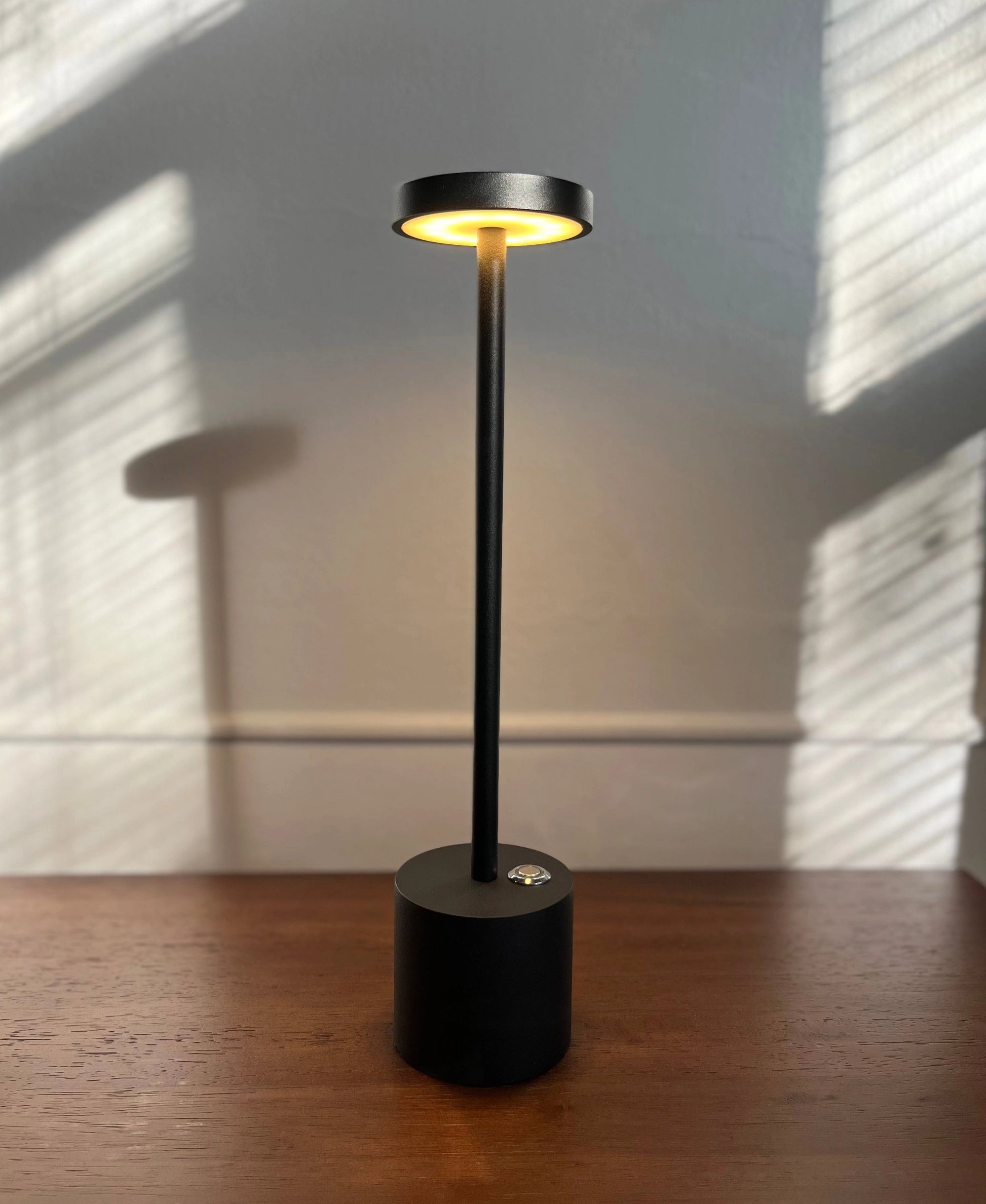 LED Portable Table Lamp with Resilient Design featuring a wooden base and circular lampshade, placed on hardwood flooring with ceiling fixture visible in the background.